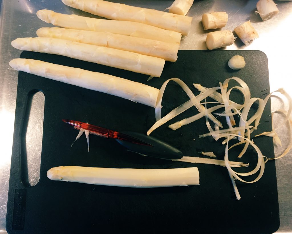 Så skalar du vit sparris. Håll den platt mot en skärbräda och skala med potatisskalare.